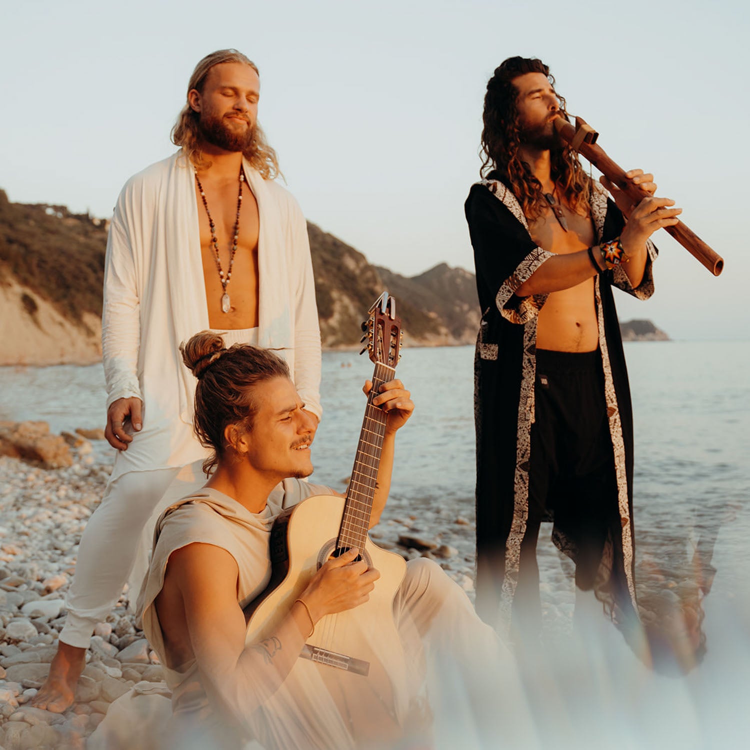 Three people playing instruments on a beach with mountains in the background