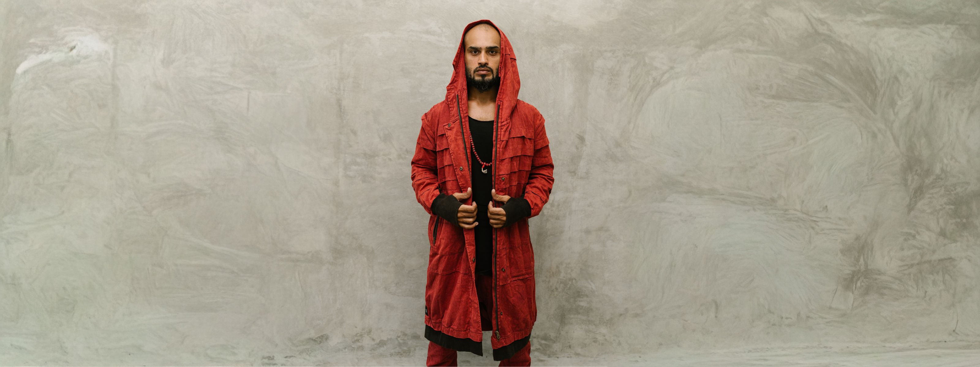 Person wearing a red hooded coat standing against a textured gray wall