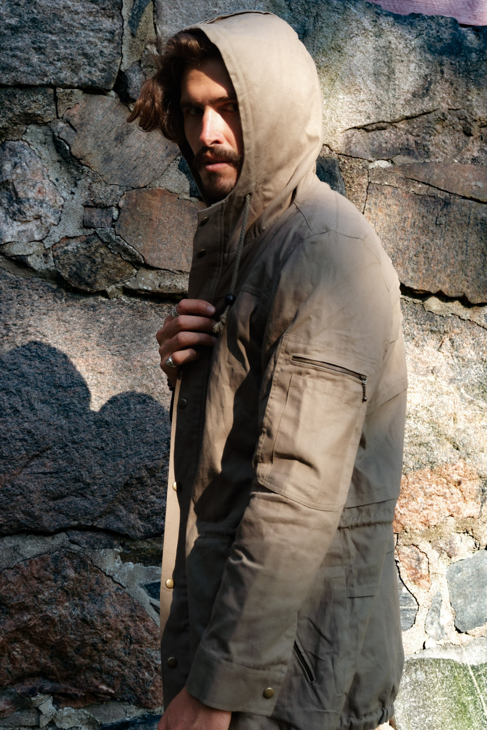 Man wearing a hooded jacket against a stone wall