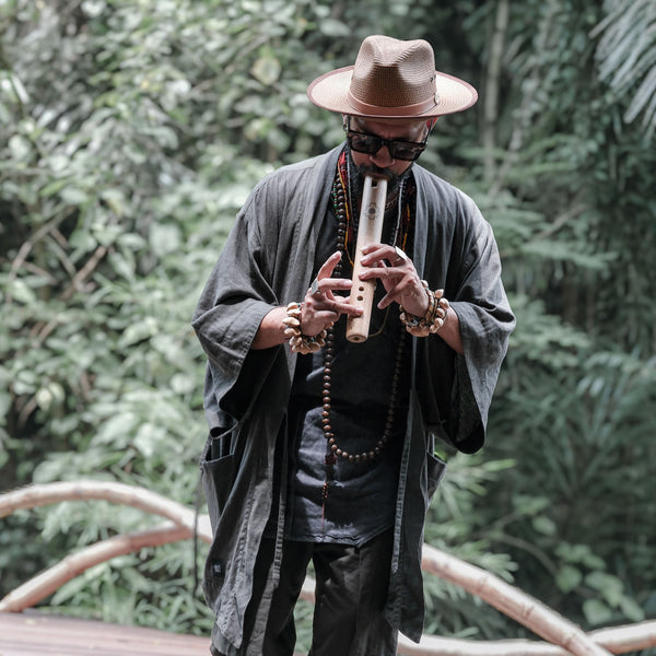 Person playing a flute in a natural setting with greenery