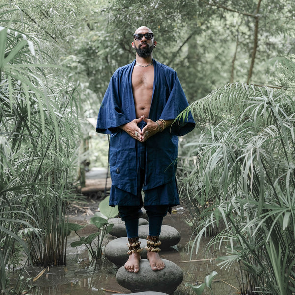 Man in a blue robe standing on stones in a forest