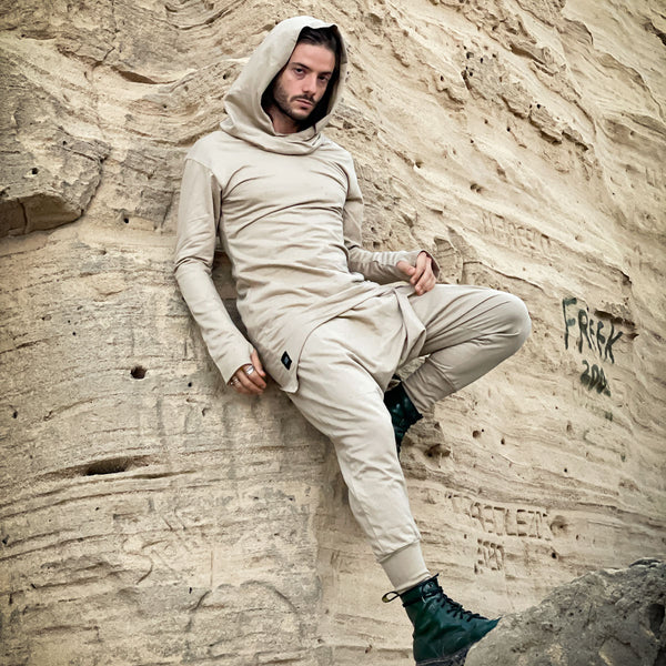 Person in beige outfit sitting against a textured wall with graffiti.