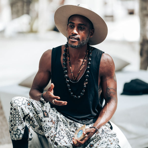 Man wearing a wide-brimmed hat and black tank top, sitting outdoors.