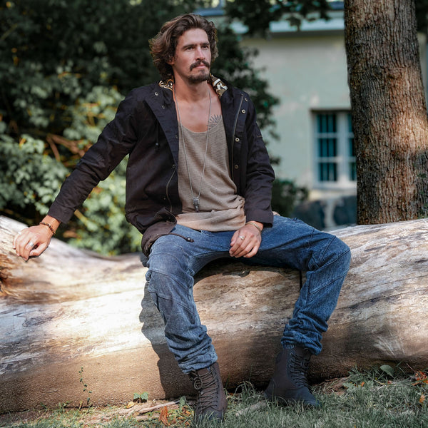 Man sitting on a log outdoors with trees and a building in the background
