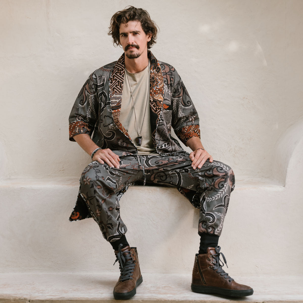 Man wearing a patterned outfit sitting on a white surface