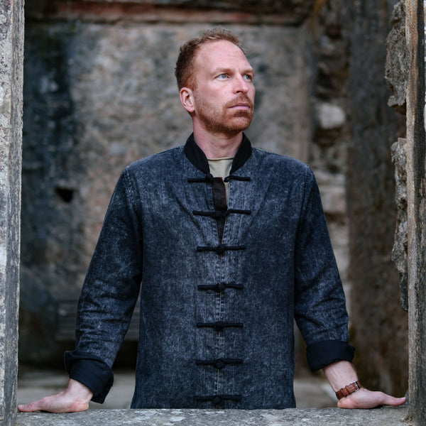 Man wearing a dark denim jacket standing in a stone archway.