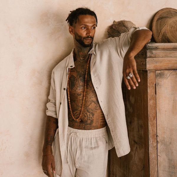 Man with tattoos leaning against a wooden cabinet with a neutral background
