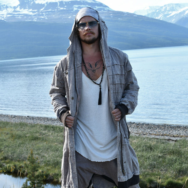 Man in a hooded jacket standing by a lake with mountains in the background