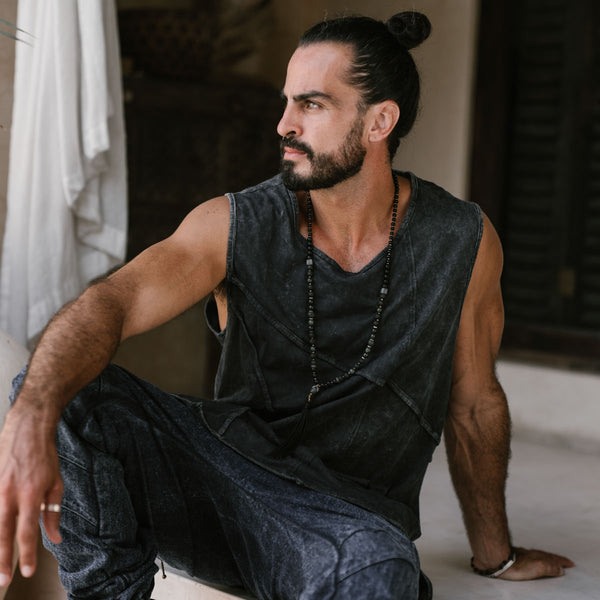 Man sitting on a step wearing a sleeveless dark shirt and pants.