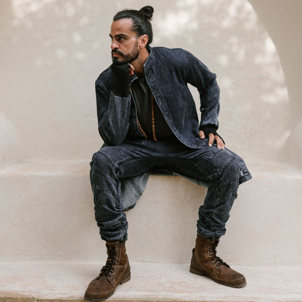 Man wearing a denim outfit with brown boots sitting on a white surface.
