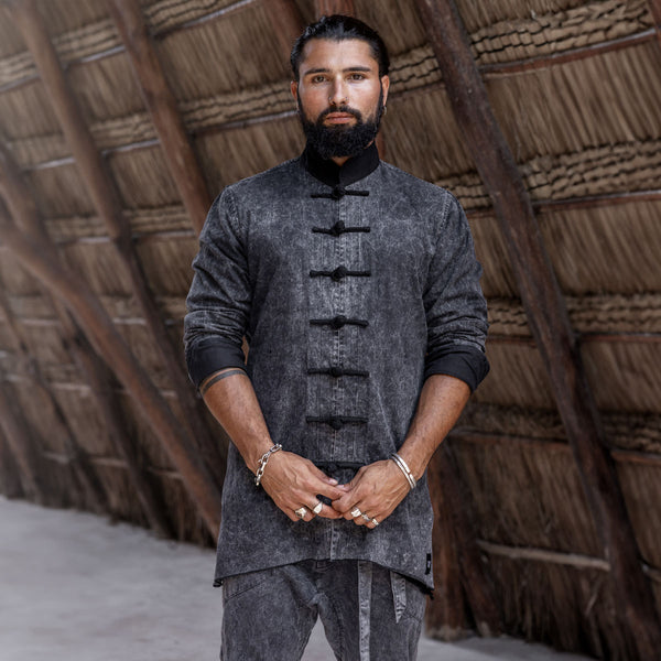 Man wearing a dark gray traditional outfit with black buttons against a wooden background