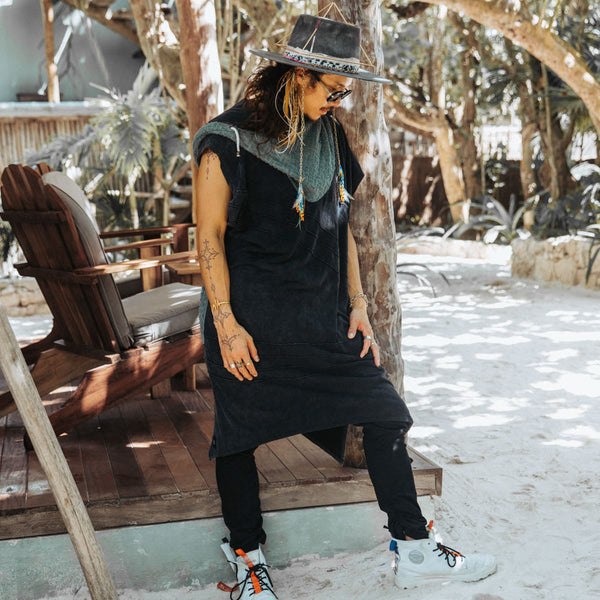 Person wearing a black outfit with a hat and sunglasses, standing in a snowy outdoor setting.