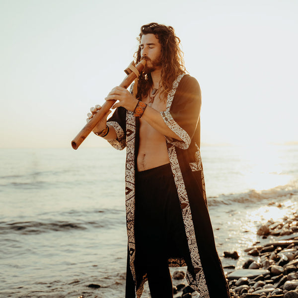 Man playing a flute by the water with a warm, natural light effect