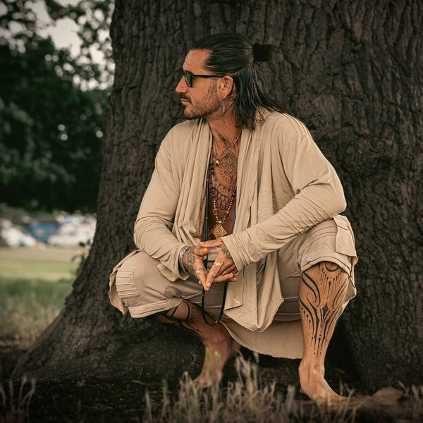 Man with tattoos sitting against a tree in a natural setting