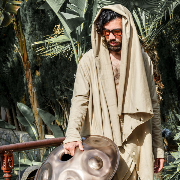 Man in a beige robe holding a handpan against a natural background